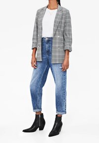 Szara kraciasta marynarka dwurzędowa, zestawiona z luźnymi niebieskimi dżinsami oraz czarnymi botkami o fakturowanym wzorze.
