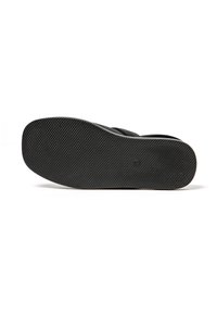 Calzado negro con suela de goma texturizada y un sutil detalle de logo. La forma es plana con una superficie superior lisa.