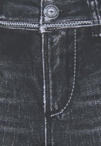 Schwarzer Denim-Stoff mit einem abgenutzten Look, der weiße Nähte, einen Reißverschluss und ein kreisförmiges Kangaroos-Logo am Bund aufweist.