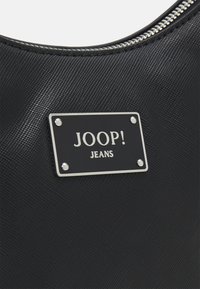 Czarna torebka teksturowana z metalową plakietką z napisem "JOOP! JEANS" przymocowaną srebrnymi nitami, z zamkiem błyskawicznym.
