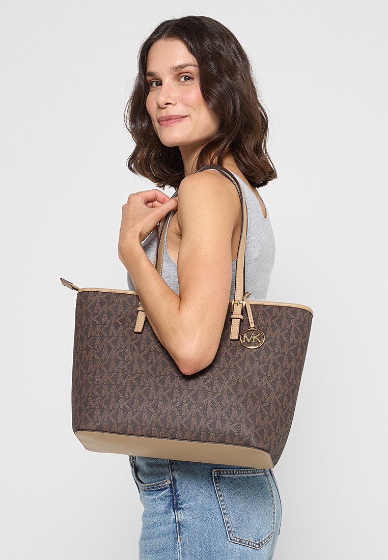 Bruine tote bag met een logo, featuring een monogram patroon in een donker en licht bruin kleurenschema, geaccentueerd met beige afwerking en rits.