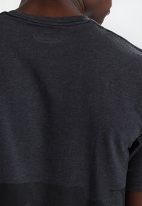 Camiseta de manga corta gris oscuro, textura suave, cuello redondo, patrón sutil en degradado en el dobladillo, sin logotipo ni detalles visibles.