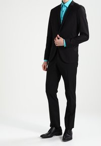 Zwart pak met een getailleerd ontwerp, gecombineerd met een turquoise overhemd. Heeft een notch lapel, slim-fit broek en zwarte nette schoenen.