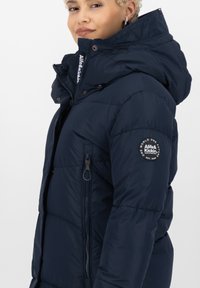 Giacca puffer navy con cappuccio e tasca con zip, dotata di una toppa con logo sulla manica e un design a trapunta texturizzata.