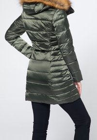 Abrigo acolchado de color verde oscuro con capucha adornada con piel sintética, silueta ajustada y textura acolchada, que llega hasta la mitad del muslo.