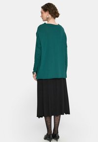 Błękitna bluzka z długim rękawem o luźnym kroju, zestawiona z czarną spódnicą do kostek. Teksturowane czarne rajstopy oraz czarne buty na niskim obcasie dopełniają całość.