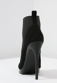 Stivali ankle neri con tacco alto, con finitura in suede, caratterizzati da un pannello elastico testurizzato, punta affusolata e un elegante tacco a stiletto.