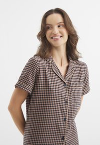 Camisa de pijama de manga corta a cuadros en azul marino y melocotón con un bolsillo, cierre de botones y detalles de cuello con ribete en contraste.