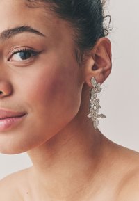 Goldfarbene Blumenohrringe mit klaren, funkelnden Edelsteinen, die ein Blattdesign zeigen und anmutig vom Ohr hängen.