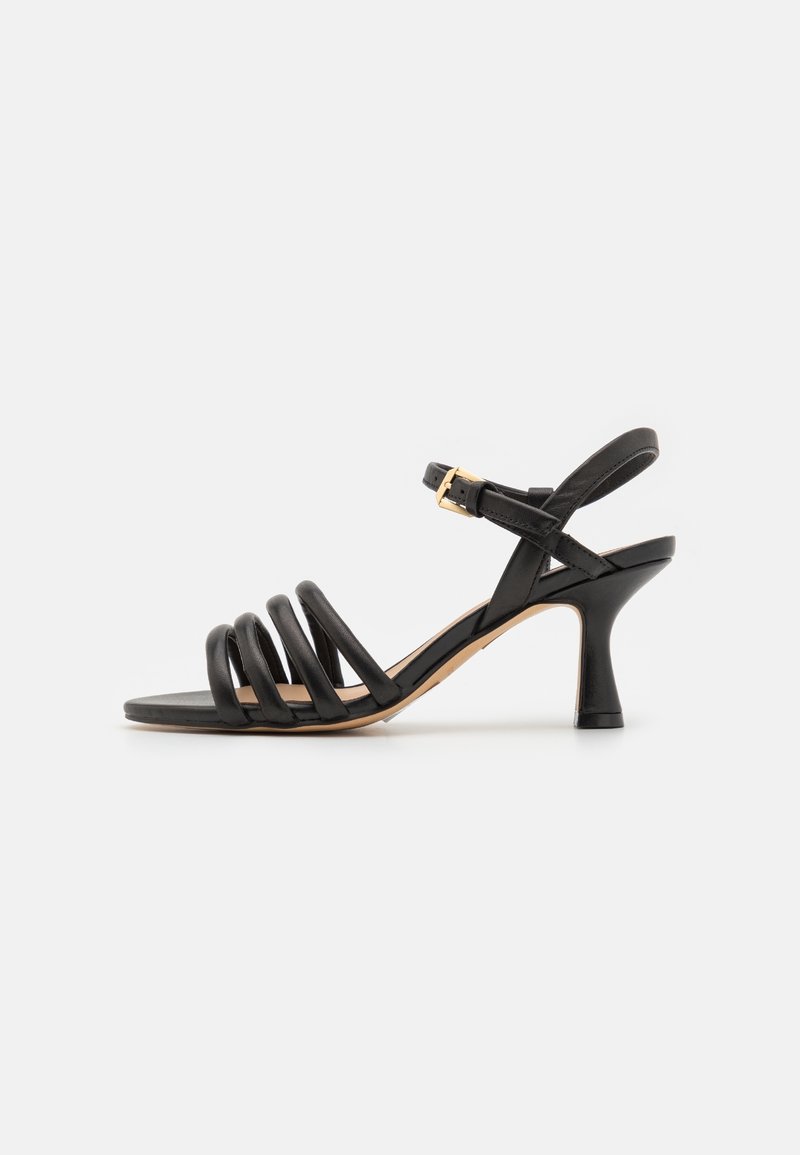 Sandale noire à talon avec quatre brides avant rembourrées, bride de cheville avec boucle dorée, et talon évasé de hauteur moyenne sur fond blanc.