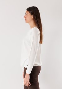 Maglione bianco a maniche lunghe con collo tondo, morbido al tatto e con spacchi laterali, abbinato a pantaloni marroni a gamba stretta. Design semplice e colori neutri.