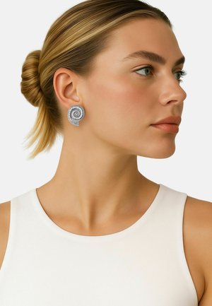 Orecchini a spirale in argento con texture rigata, che presentano un design unico a forma di conchiglia. Indossati da un modello con capelli raccolti all'indietro e abbigliamento minimal.
