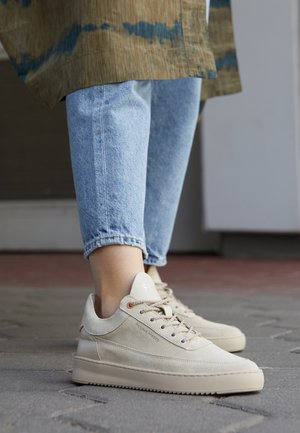 Sneakers in suede beige con superficie testurizzata, punta rotonda e lacci tonali. Presentano un'etichetta di marca bianca e una suola in gomma con scanalature.