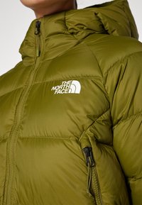 Maslinasto zelena puf jakna s džepom na zip i logotipom The North Face. Jaka je podstavljena, s visokim ovratnikom i teksturiranim materijalom.