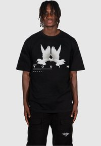 T-shirt en coton noir avec un graphique de deux colombes blanches et le texte "JEUNESSE PERDUE" en lettres audacieuses en dessous, à manches courtes et à coupe décontractée.