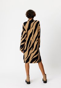 Vestito lungo fino al ginocchio con maniche lunghe, caratterizzato da un motivo a strisce di tigre beige e nere, realizzato in un tessuto morbido e con spacchi laterali.