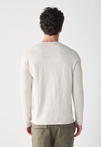 Pull long à manches longues beige clair à col rond simple, fabriqué à partir d'un tissu doux, présentant une texture lisse et une coupe décontractée à l'arrière.