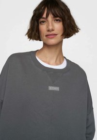 Felpa grigia con collo a girocotola a coste, caratterizzata da una piccola etichetta "10DAYS" sul petto. Tessuto morbido e design dal fit rilassato.