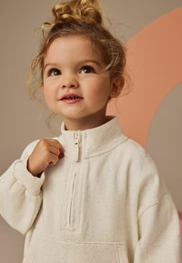 Kerman puoli-vetoketjullinen fleece-sweatshirte, jossa on pilkullinen pinta ja ribatut hihansuut. Sisältää korkean kauluksen ja kengurupussin.