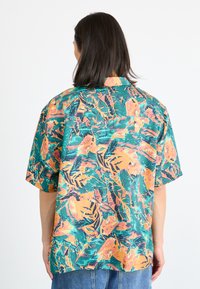 Short-sleeve shirt in vibrant green, orange, and blue. Features an abstract leaf pattern, collar, and relaxed fit with a straight hem.