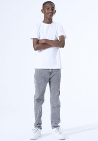 Witte katoenen t-shirt gecombineerd met grijze spijkerbroek. Sneakers zijn wit met veters. Casual fit met een relaxte silhouet, staand tegen een lichte achtergrond.