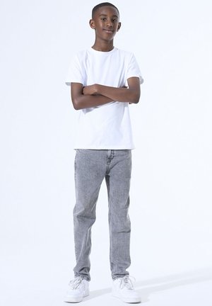 Witte katoenen t-shirt gecombineerd met grijze spijkerbroek. Sneakers zijn wit met veters. Casual fit met een relaxte silhouet, staand tegen een lichte achtergrond.