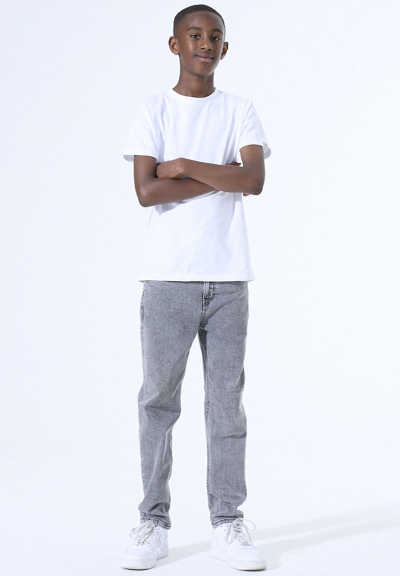 Witte katoenen t-shirt gecombineerd met grijze spijkerbroek. Sneakers zijn wit met veters. Casual fit met een relaxte silhouet, staand tegen een lichte achtergrond.