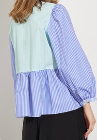 Helles blaues, gestreiftes Bluse mit Puffärmeln, die einen gerafften Saum und ein kontrastierendes mintgrünes Panel auf der Rückseite hat.