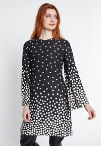 Schwarzes Kleid mit Polka-Dots und langen Ärmeln, das ein Verlaufsmuster aus weißen Punkten aufweist. Weicher Stoff, lockere Passform und runder Ausschnitt.