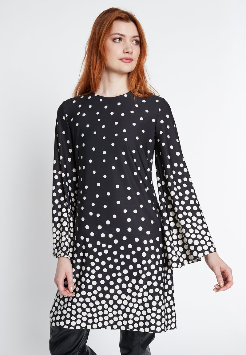Schwarzes Kleid mit Polka-Dots und langen Ärmeln, das ein Verlaufsmuster aus weißen Punkten aufweist. Weicher Stoff, lockere Passform und runder Ausschnitt.