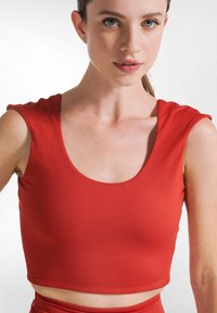 Top rosso accorciato con scollatura a barca e maniche corte, leggermente imbottite. Il tessuto appare liscio con un design aderente.
