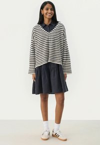 Stripet striktrøje i creme og marineblå, løs pasform, V-hals. Sammen med en marineblå lagkjole. Båret med hvide sneakers og ankelstrømper.