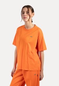Pomarańczowa bawełniana koszulka z okrągłym dekoltem i krótkimi rękawami, z małym logo na piersi i luźnym krojem.