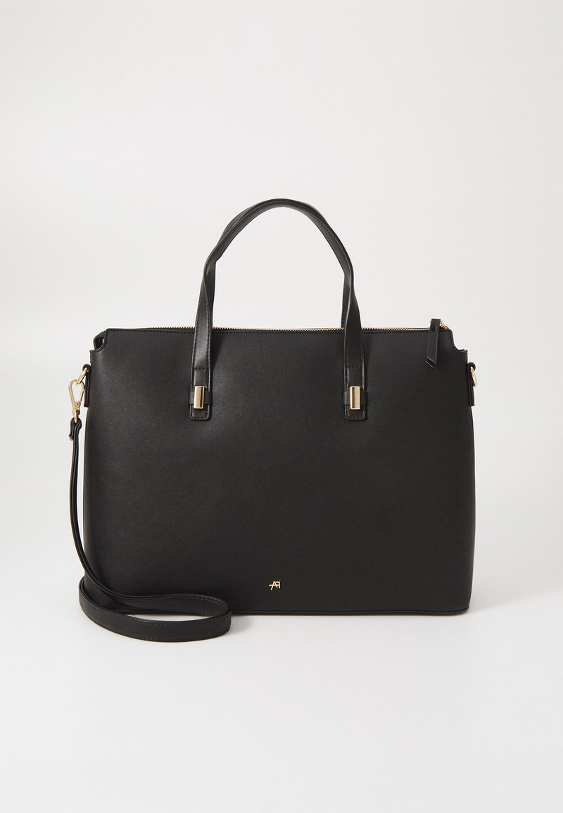 Sac à main structuré noir avec deux poignées supérieures, ferrures dorées, une bandoulière amovible et une fermeture zippée sur fond blanc.
