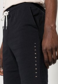 Černé bavlněné šortky s bočními kapsami, vybavené bílou šňůrkou na stažení a logem "JACK & JONES" v kontrastní barvě podél strany.