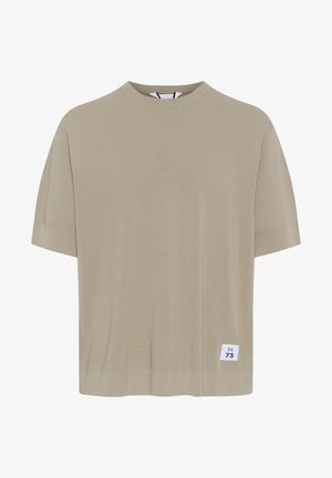 Krátky rukáv, béžové tričko vyrobené z jemného materiálu. Disponuje okrúhlym výstrihom a malou bielou nášivkou s nápisom "M73" na dolnej ľavej strane.