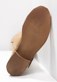 Brown suede boot with a textured upper, featuring a wooden sole embossed with a butterfly logo and a side zipper for closure.