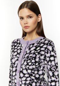 Cardigan a maglia con una base nera e un motivo astratto in lavanda e bianco, chiusure con bottoni viola e scollatura rotonda.