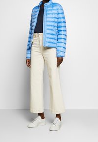 Lysblå pufferjakke med vandret syninger, parret med off-white vide bukser og hvide sneakers. Enkel rund halsudskæring.