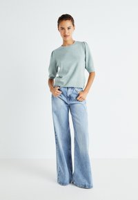 Pull en tricot bleu clair avec des manches courtes bouffantes, associé à un jean en denim clair à jambes larges. Design simple avec des poignets et un ourlet côtelés.