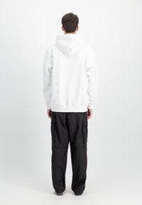 Biely mikina s kapucňou a klokankou, v kombinácii s čiernymi cargo nohavicami so bočnými vreckami a voľnejším strihom.