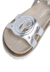 Silverfärgade lädersandaler med en cirkulär dekorativ detalj, mjukt beige fotbädd och en texturerad vit sula för bra grepp.