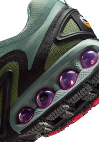 Scarpa sportiva verde e nera con tomaia testurizzata, collarino imbottito e grandi cuscinetti di ammortizzazione ad aria viola su una suola segmentata.