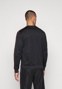 Sudadera deportiva negra con cuello redondo, con rayas rojas a lo largo de los hombros. Fabricada con un tejido suave y elástico.