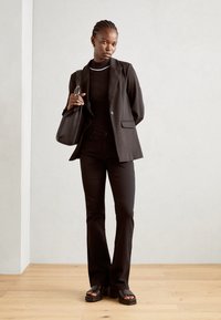 Zwarte op maat gemaakte blazer, zwart lang mouwen top en flare broek met een slim fit. Gecombineerd met een zwarte handtas en platform sandalen.