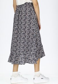 Blumiger Midirock mit navy Hintergrund, der kleine weiße und pinke Blumen zeigt. Ausgestellter Saum und geraffter Taillenbund. Getragen mit weißen Sneakers.