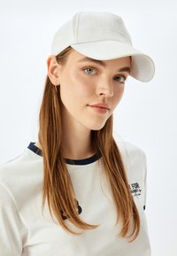 Hvid baseballkasket med en tekstureret frontpanel og buet skygge, parret med en lys t-shirt med en marineblå krave og tryk.