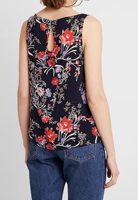 Top senza maniche floreale blu marina con motivi rossi e viola, caratterizzato da un'apertura a goccia sulla schiena e un design a vestibilità rilassata. Abbinato a jeans a vita alta.