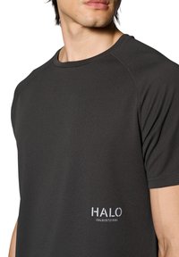 Czarna koszulka sportowa z teksturowanej tkaniny, okrągłym dekoltem oraz białym nadrukowanym logo po lewej stronie z numerami poniżej.