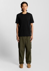 Sort bomulds T-shirt med rund hals, parret med grønne cargo bukser med sidelommer og brune slip-on sko.